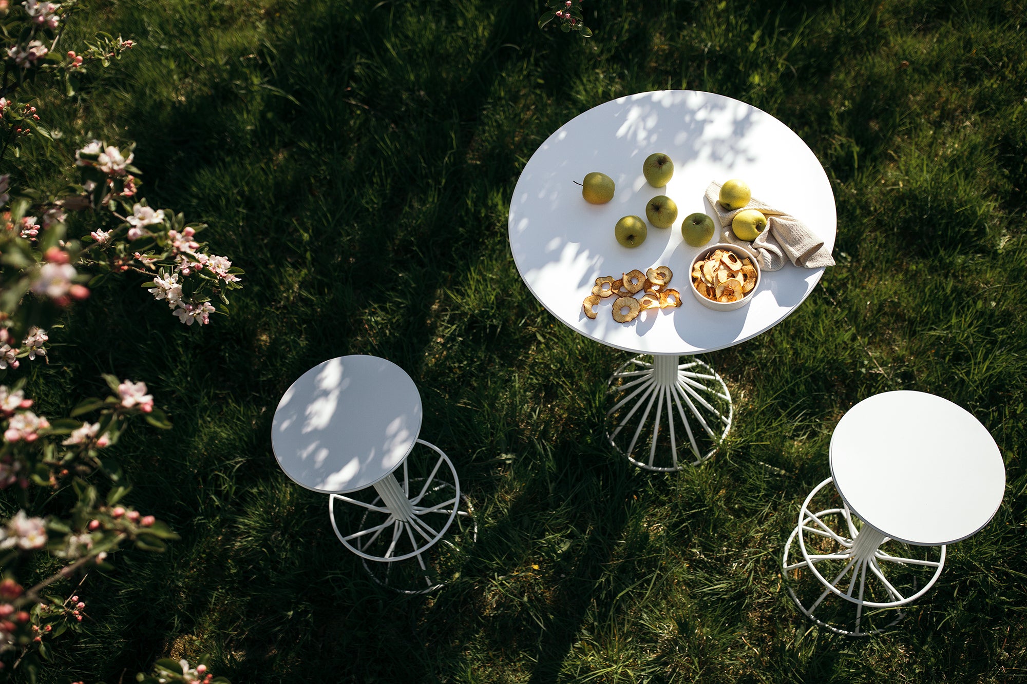 Roots Utemöbler i vitt ståendes i en grönskande äppleträdgård.