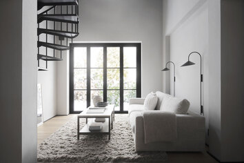 Orwel Soffbord i Brunlackad Ek / Travertin i en modernt vardagsrum med vita väggar och svart fönster. Soffbordet står på en fluggif ryamatta och kombineras med Duncan Soffa.