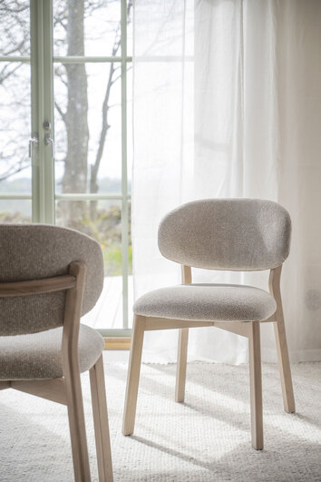 Patterson stol i vitpigmenterad ek med beige tyg framför fönster med skira gardiner