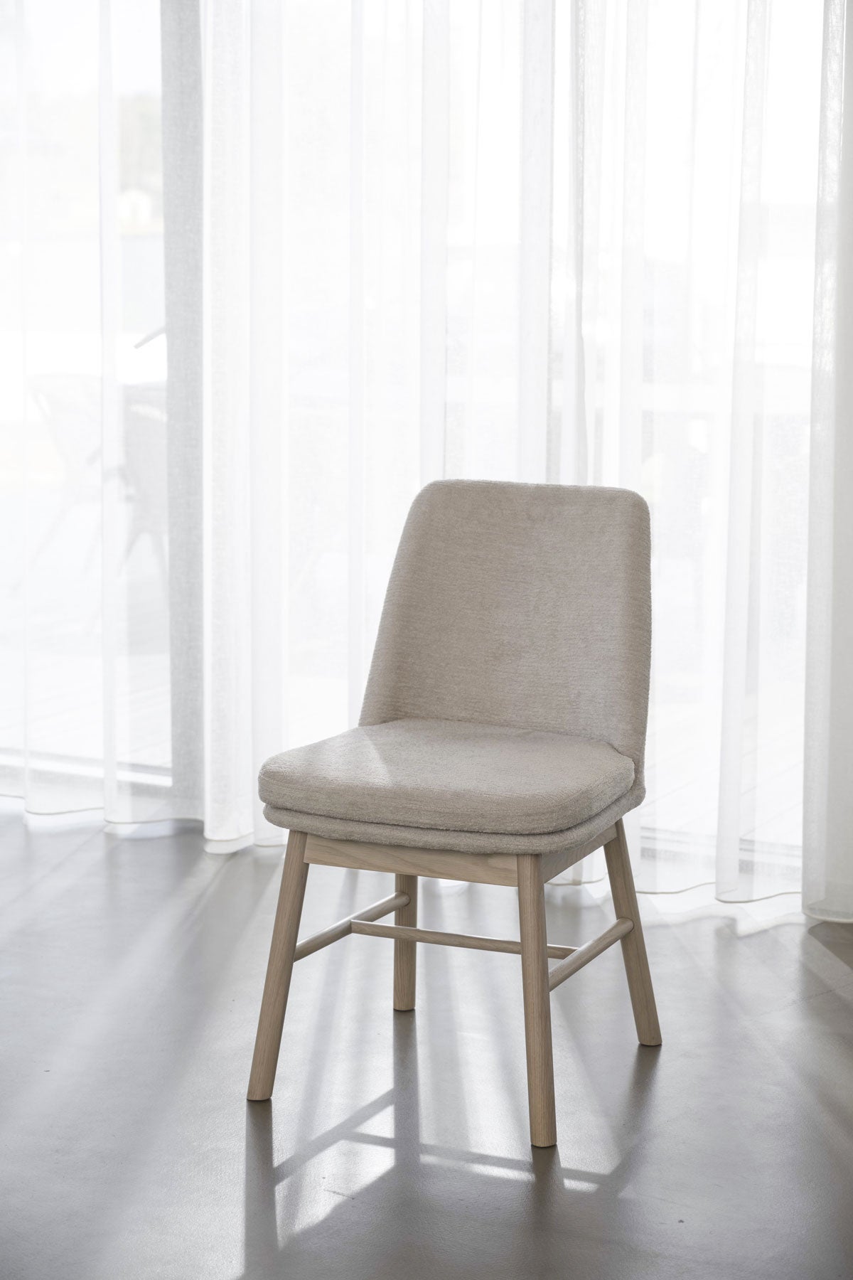 Amesbury Stol Vitpigmenterad Ek i ljusbeige tyg framför skira gardiner