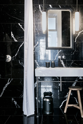 Vipp badrums inredning i ett svart kaklat badrum med vit kommod. På den vita kommoden står Vipp 7 Tandborsthållare och tvålpump i svart. Under finns en pedal hink i svart. 