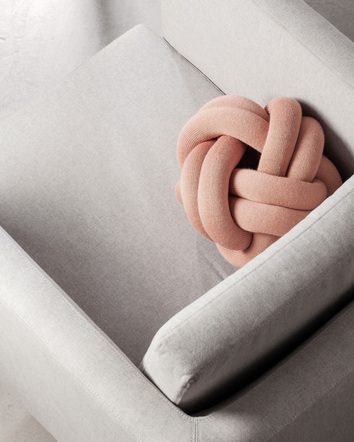 Knot Cushion i färgen Dusty Pink i grå fåtölj