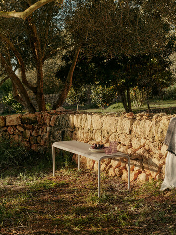 Dapple Bänk i färgen Cashmere mot en stenmur i solnedgången