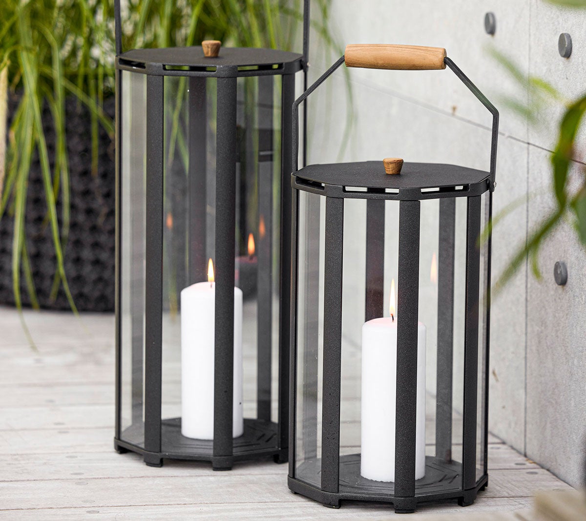 Lightlux lykta i storlek small och stor med tänt stearinljus på altan