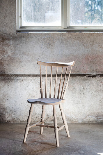 Classic Pinnstol i klarlackad björk i ett rum med rå betongvägg och ett fönster som släpper in dagsljus