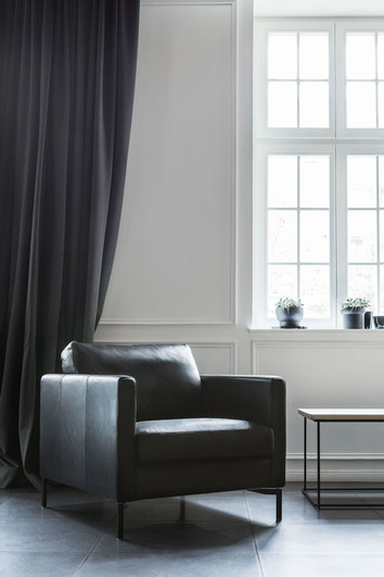 Impulse Fåtölj i läder framför en mörk gardin