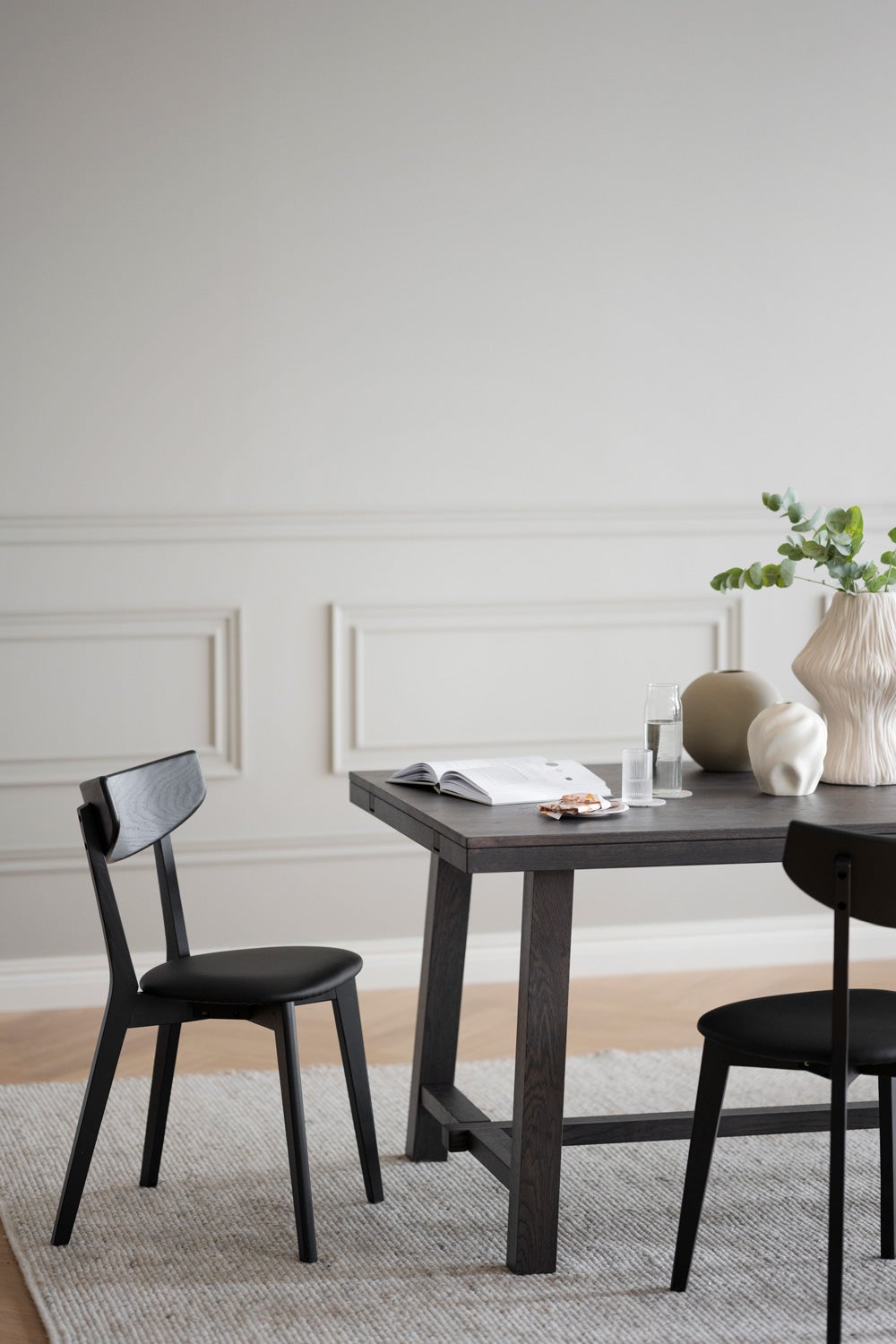 Ami Stol i svartbetsad ask vid ände av rektangulärt matbord på ullmatta