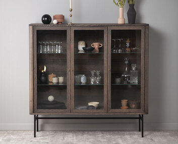 Miljöbild på Velvet vitrinskåp med krukor och vaser bakom de vackra glasdörrarna.