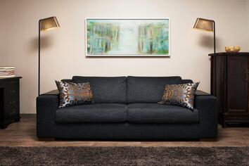 Två Owalo 7010 Golvlampa Svart på varsin sida av en svart soffa med metalliska prydnadskuddar