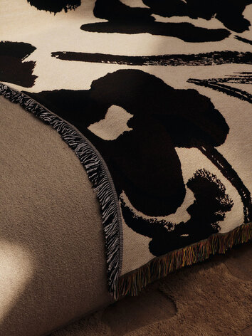 Cilla Tapestry Pläd i färgen Off-White/Dark Grape som ligger slängd över en soffkant