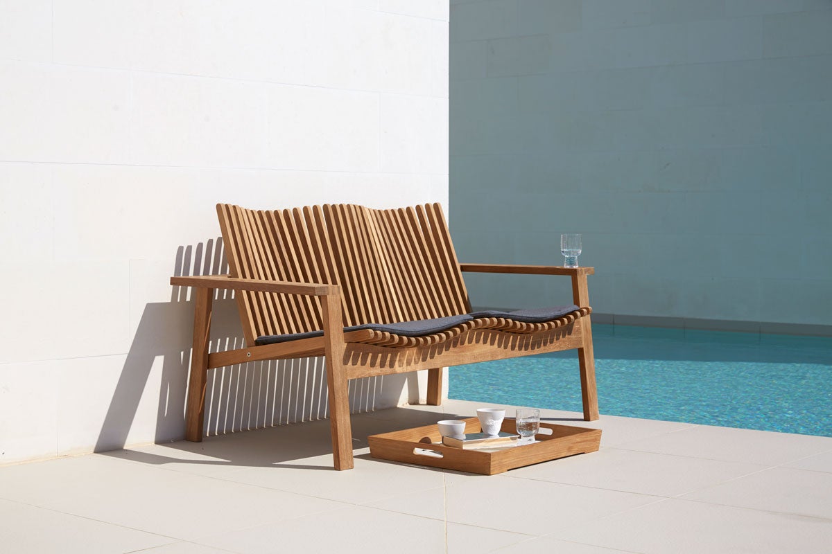 Amaze 2-Sits Soffa intill en pool. Det står en uppdukad bricka framför soffan.