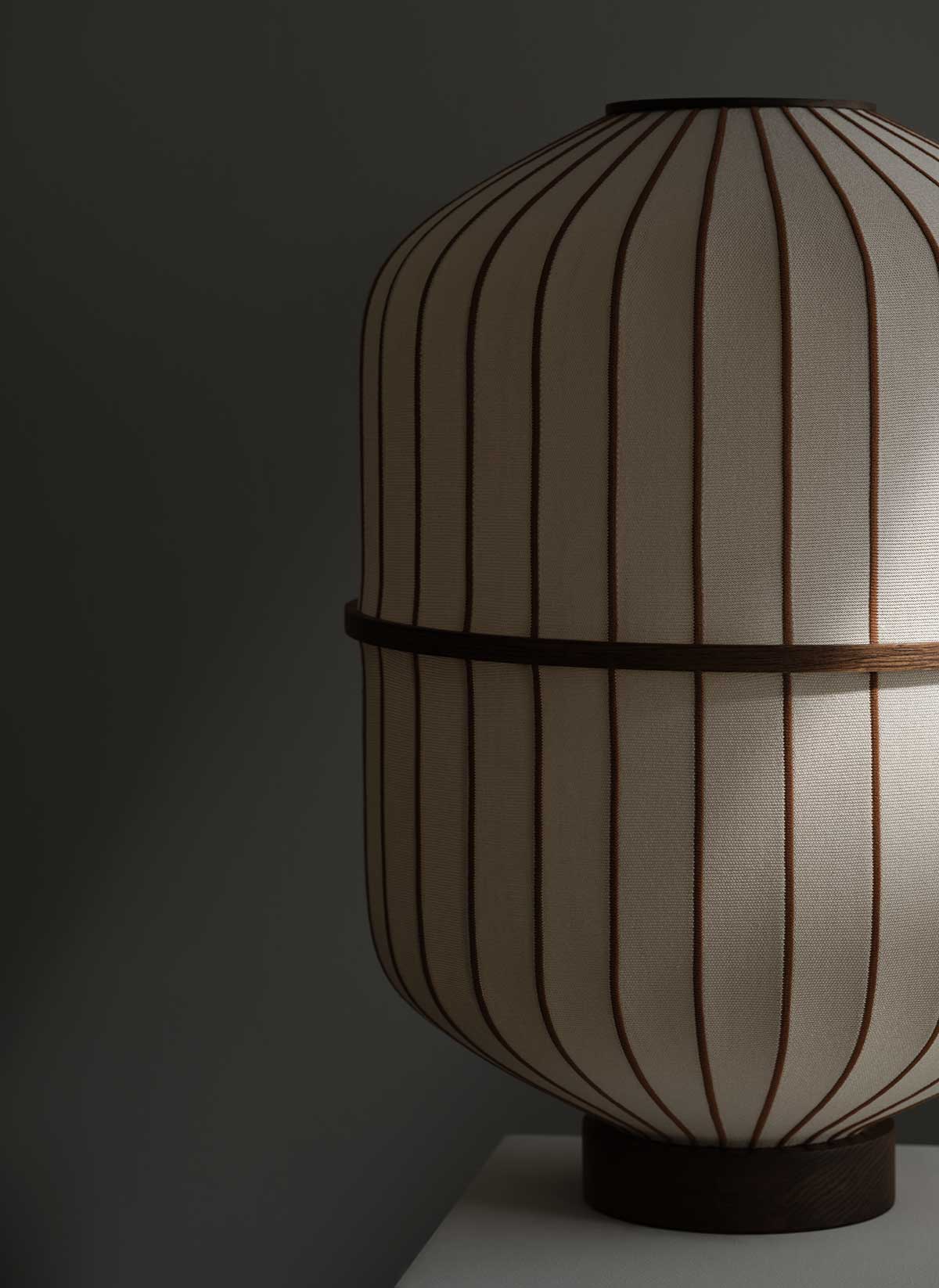 Bolia-Lucen-Table-Lamp-Sand-Dark-Oiled-Oak-Lifestyle-1.jpg Lucen bordslampa i mörkoljad ek i ett dunkelt rum där en strimma av ljus lyser in.