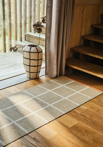 Criss Gångmatta i färgen Beige framför ett fönster med en rutig kruka