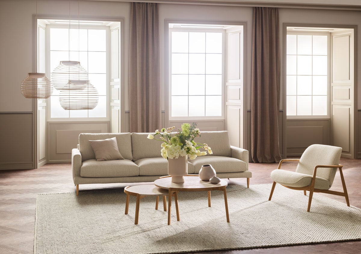 Veneda Soffa 4-sits i ett ljust tyg i ett vardagsrum med vackert ljusinsläpp och moderna möbler.