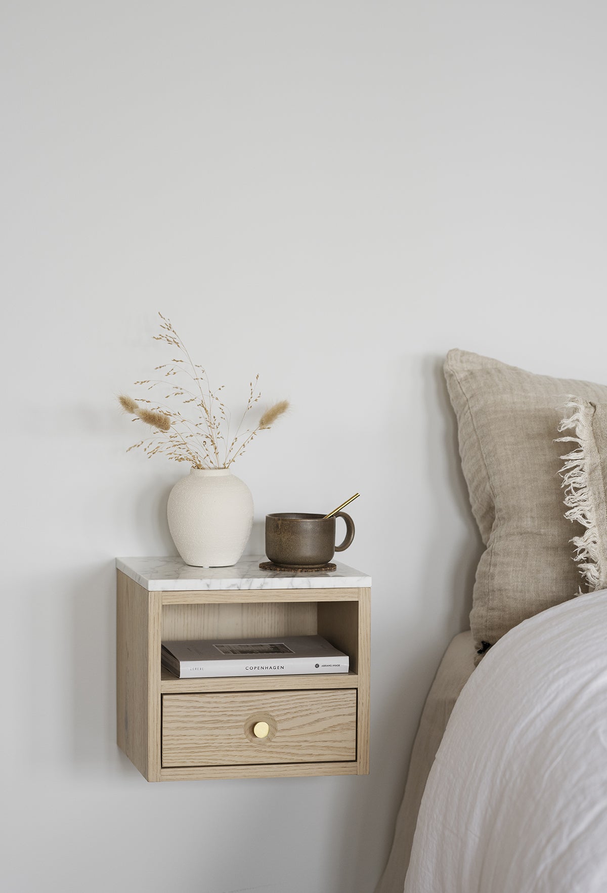 Whitmore Sängbord bredvid säng med en kruka, en kopp och en bok