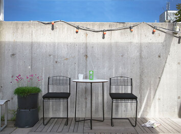 High Tech Stol Svart runt High Tech Bord 60 mot betongvägg på soligt trädäck