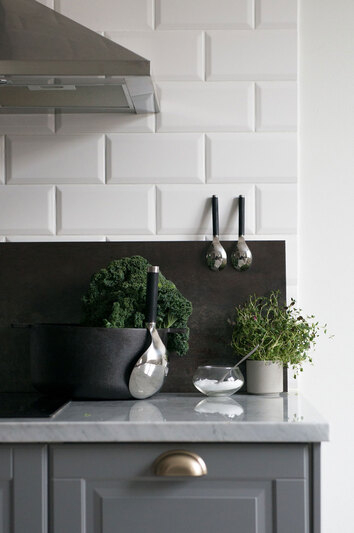 Salvia serveringssked framme på köksbänken bredvid krukor med gröna örter, i ett modernt kök med blå luckor och marmorbänkskiva.