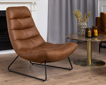 Milford loungefåtölj i Cognac ståendes bredvid sidobord. 