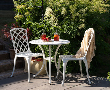 Arras Cafébord Vit med två stolar framför buskage 
