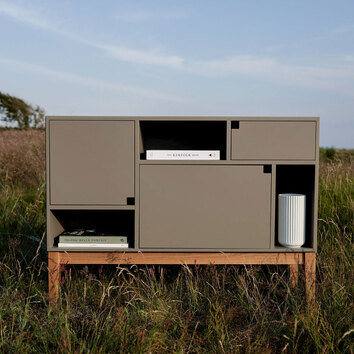 Citti Skåp i färgen Mole Grey. Skåpet står utomhus under blå himmel och i facken står och ligger inredningsdetaljer. 