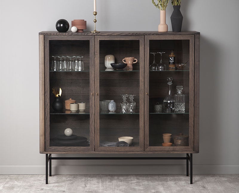 Miljöbild på Velvet vitrinskåp med krukor och vaser bakom de vackra glasdörrarna. 