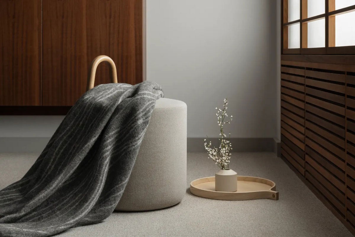 Fanér Pläd på grå puff bredvid en bricka med en vas