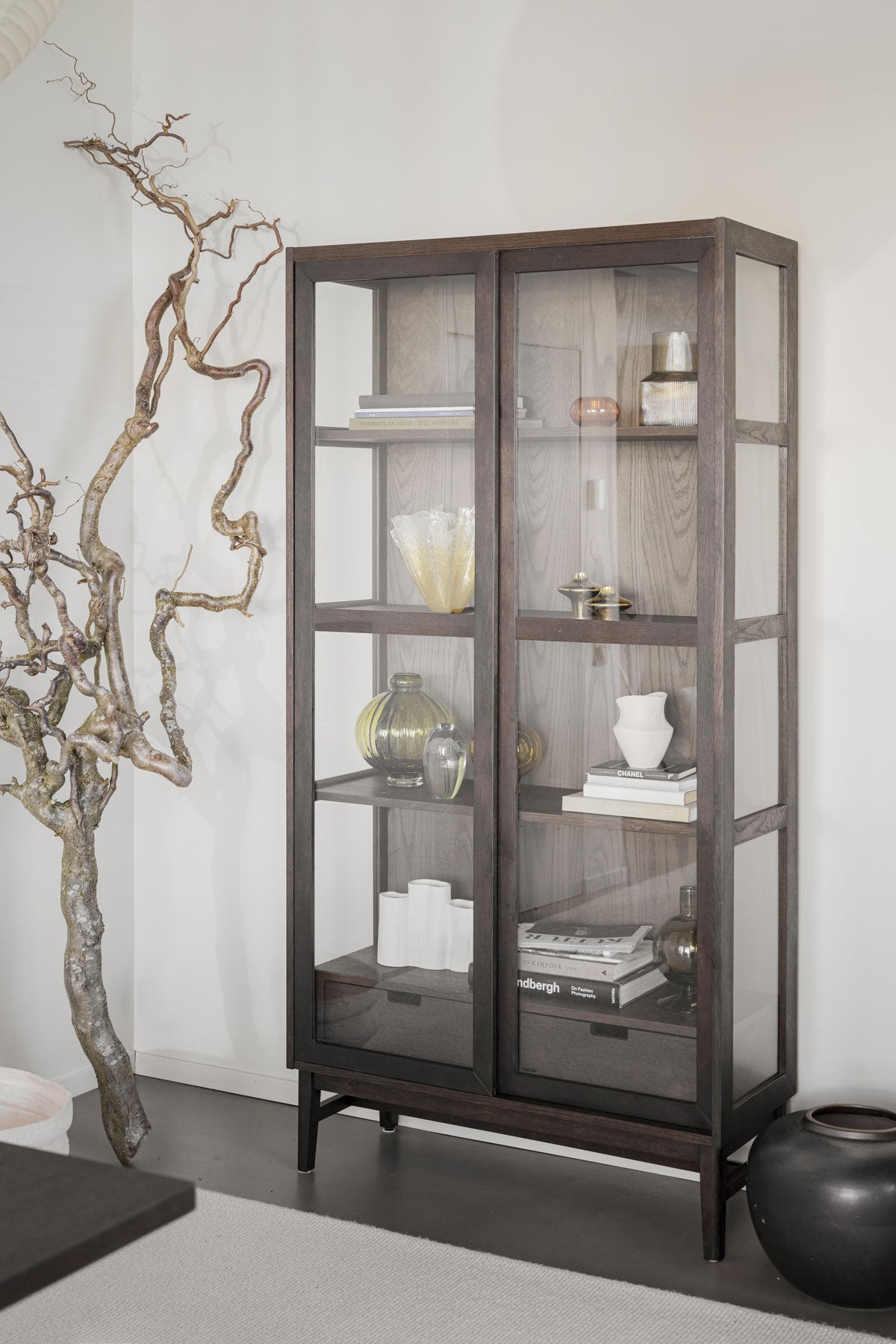 Hazelton Vitrinskåp i brun ek bredvid en stor trädgren som dekoration