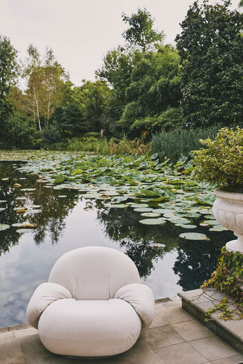 Pacha Outdoor Lounge Chair med Armstöd ståndes på en terras brevid en näckrosdamm. 