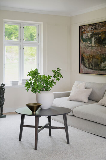 Filippa Soffbord 90 i brun ek i vardagsrum. Bordet är dekorerat med en skål och gröna kvistar.