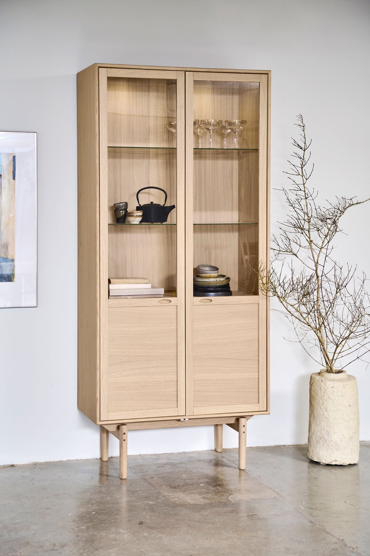 Aeris Vitrinskåp med dekorativa detaljer intill kruka med växt