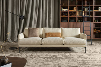 Soffan Ravel i fyrsitsmodell, stående i vardagsrumsmiljö. Soffan är klädd i ett ljust tyg.