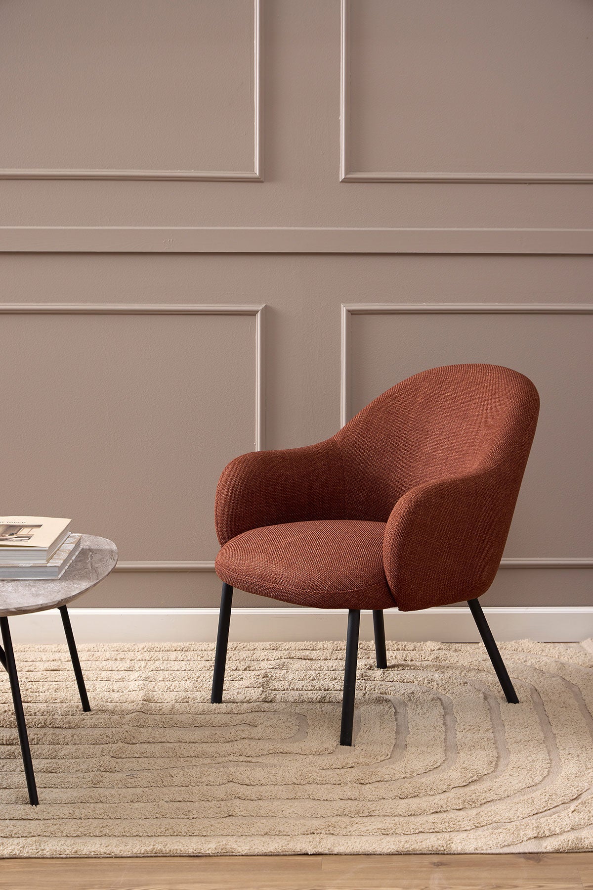 Spencer Loungefåtölj i tyget Basel Terrakotta som står på en beige ullmatta