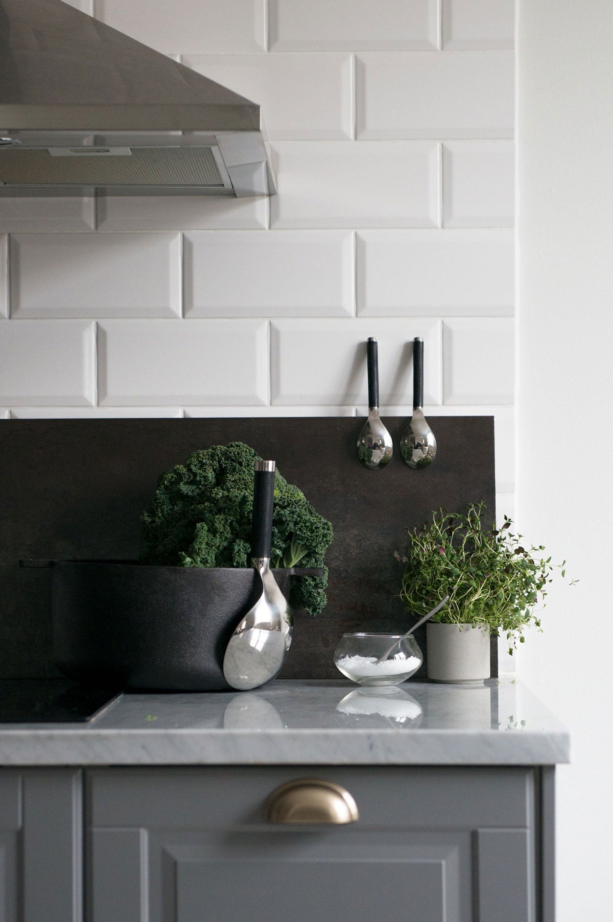 Salvia serveringssked framme på köksbänken bredvid krukor med gröna örter, i ett modernt kök med blå luckor och marmorbänkskiva.