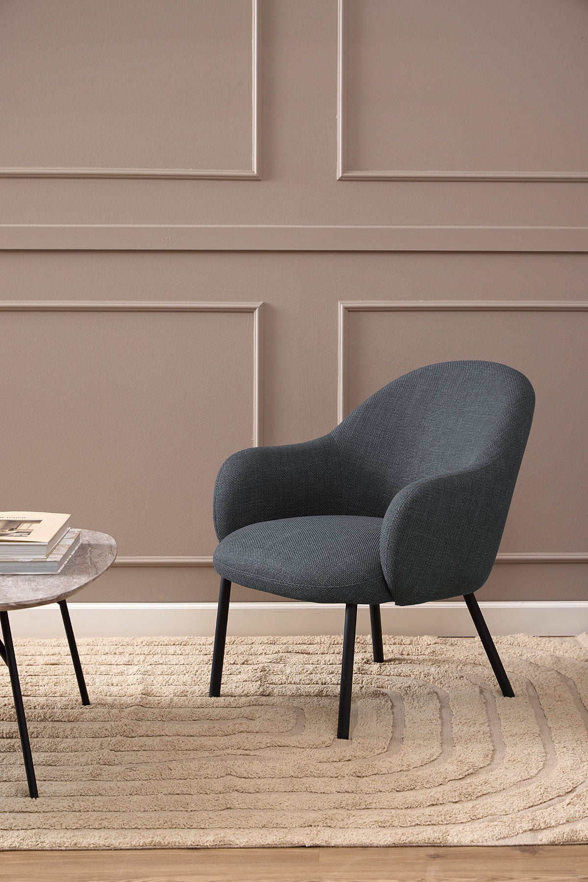 Spencer Loungefåtölj i tyget Basel Mörkgrå som står på en beige ullmatta
