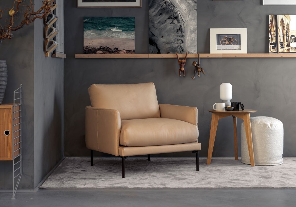 Fåtöljen Ravel från Furninova klädd i ett ljust läder, stående i vardagsrumsmiljö. 