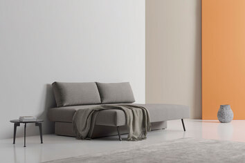 Osvald Bäddsoffa i tyget 282 Avella Warm Grey i utfällt läge med grå pläd