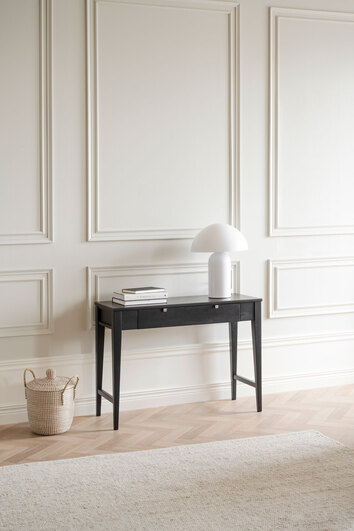 Confetti Avlastningsbord i svartlack intill vägg med en vit bordslampa och böcker på hög