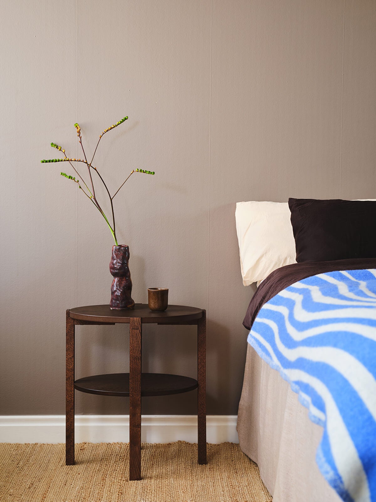 Solo Fåtöljbord i rökt ek, bredvid en bäddad säng