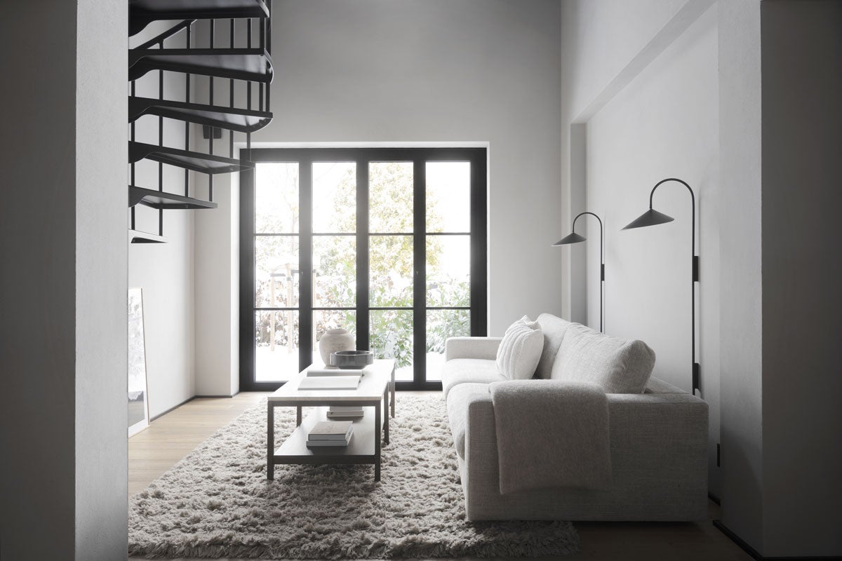 Orwel Soffbord i Brunlackad Ek / Travertin i en modernt vardagsrum med vita väggar och svart fönster. Soffbordet står på en fluggif ryamatta och kombineras med Duncan Soffa.