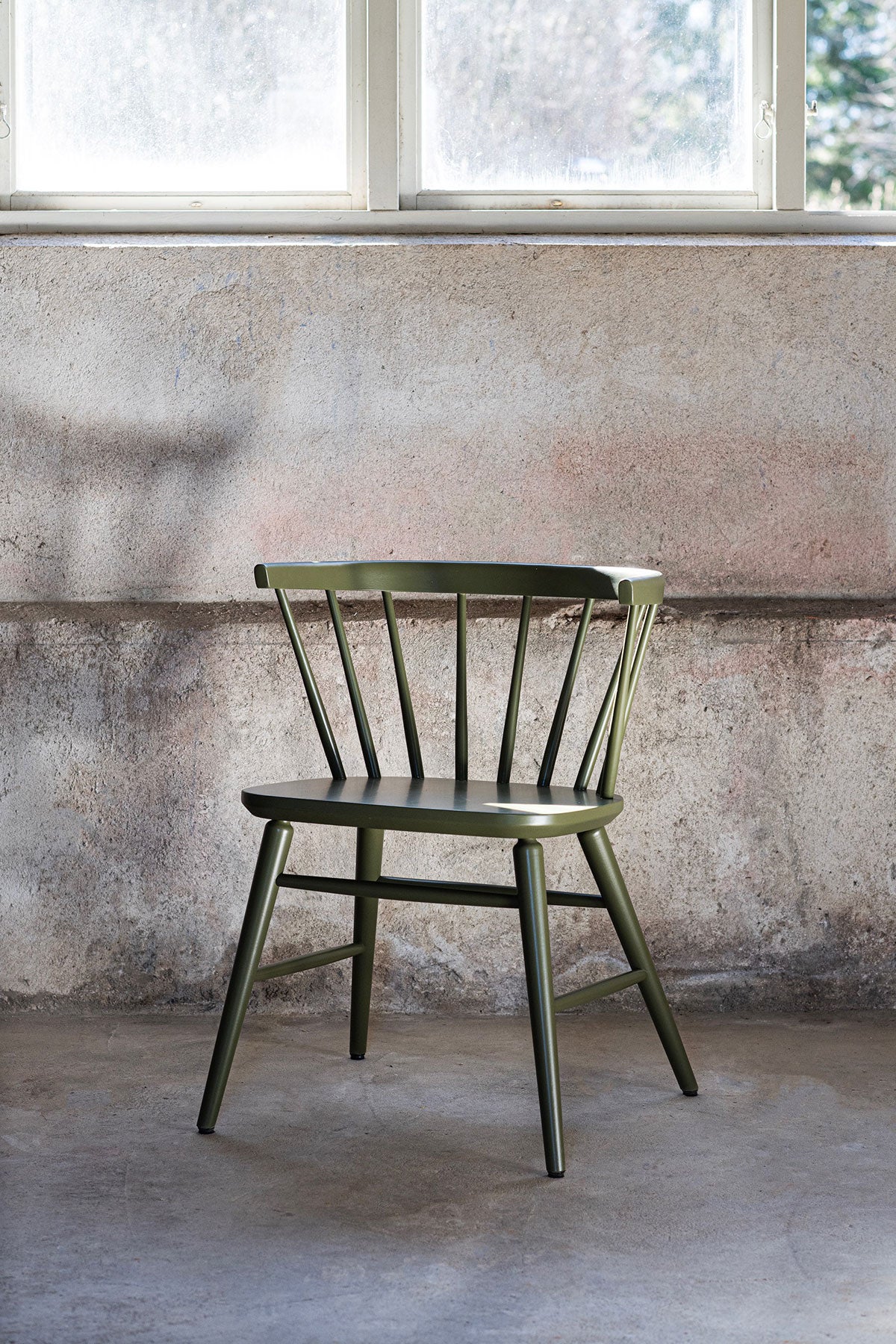Florida Karmstol i Wigellsgrön lack i ett rum med rå betongvägg och ett fönster som släpper in dagsljus