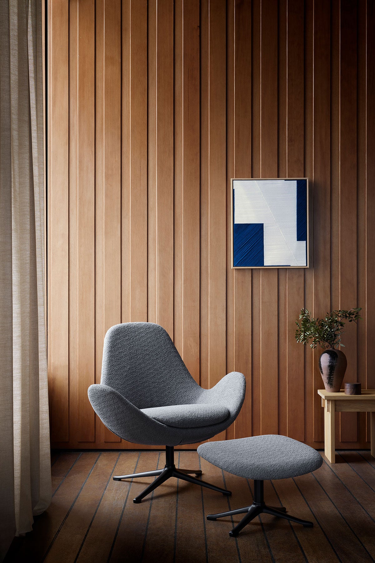 Ghost Low Fåtölj och fotpall i tyget Bormio Soft Grey med ben i svart aluminium i rum med träklädda väggar