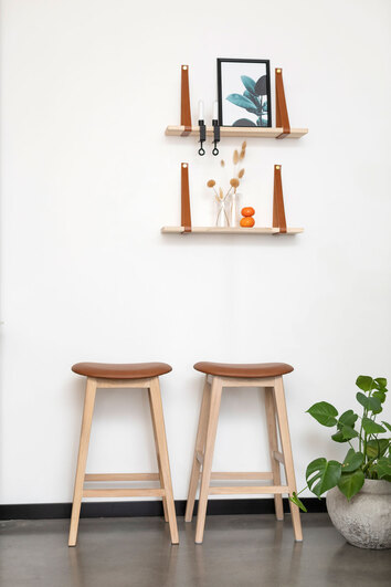 Två stycken Kyoto barpallar i vitoljad ek med lädersits i Cognac stående under två vägghyllor med dekorativa detaljer