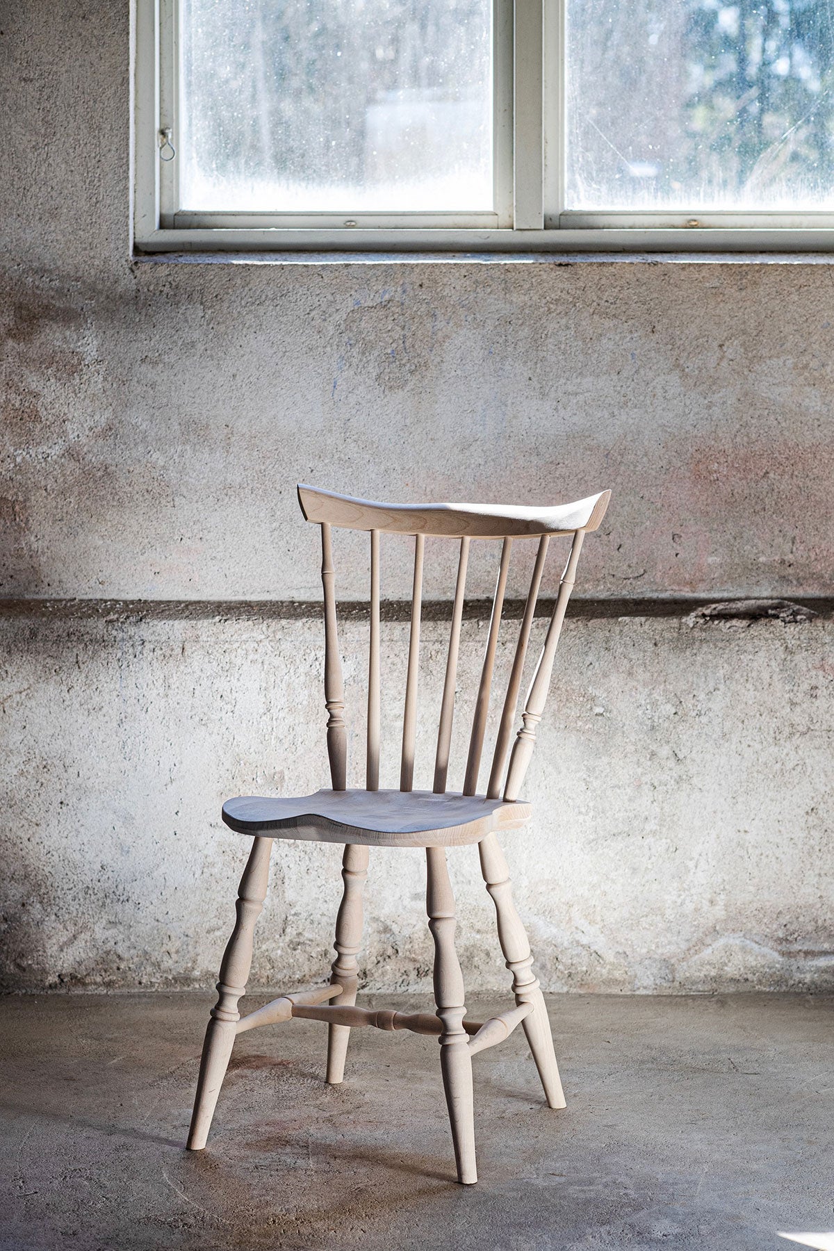 Classic Pinnstol i klarlackad björk i ett rum med rå betongvägg och ett fönster som släpper in dagsljus
