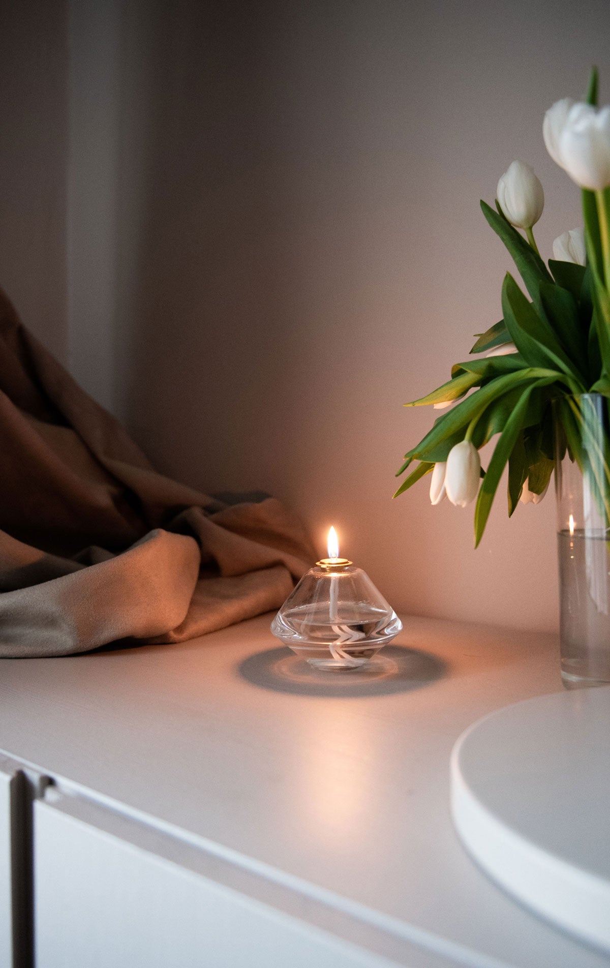 Aki oljelampa som brinner mysigt på ett sideboard med tulpaner 