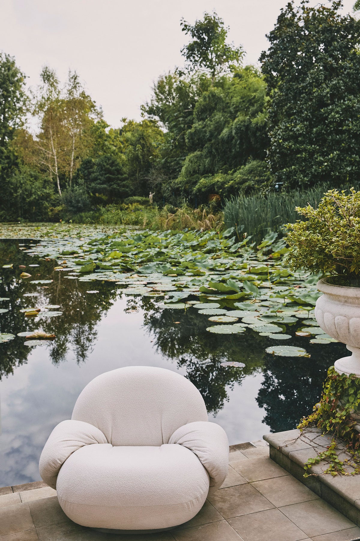 Pacha Outdoor Lounge Chair med Armstöd ståndes på en terras brevid en näckrosdamm. 