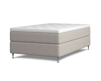 Kontinentalsängen Harmoni. Bilden visar Harmoni med en bredd av 120 centimeter. Sängen är klädd i beige tyg. Benen är av förkromat stål.