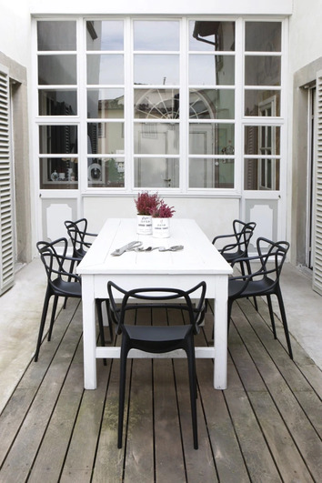 Masteras Stolar o svart runt ett vitt bord på en uteplats vid medelhavet. 