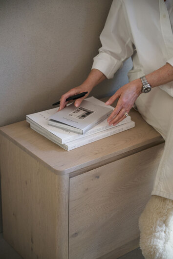 Melstone Sideboard i höjd 50 centimeter i vitpigmenterad ek med en kvinna som håller i en trave böcker