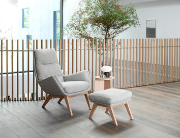 Moro Fåtölj och fotpall i tyget Brescia Calm Grey med ben i ek i ljus kontorsmiljö