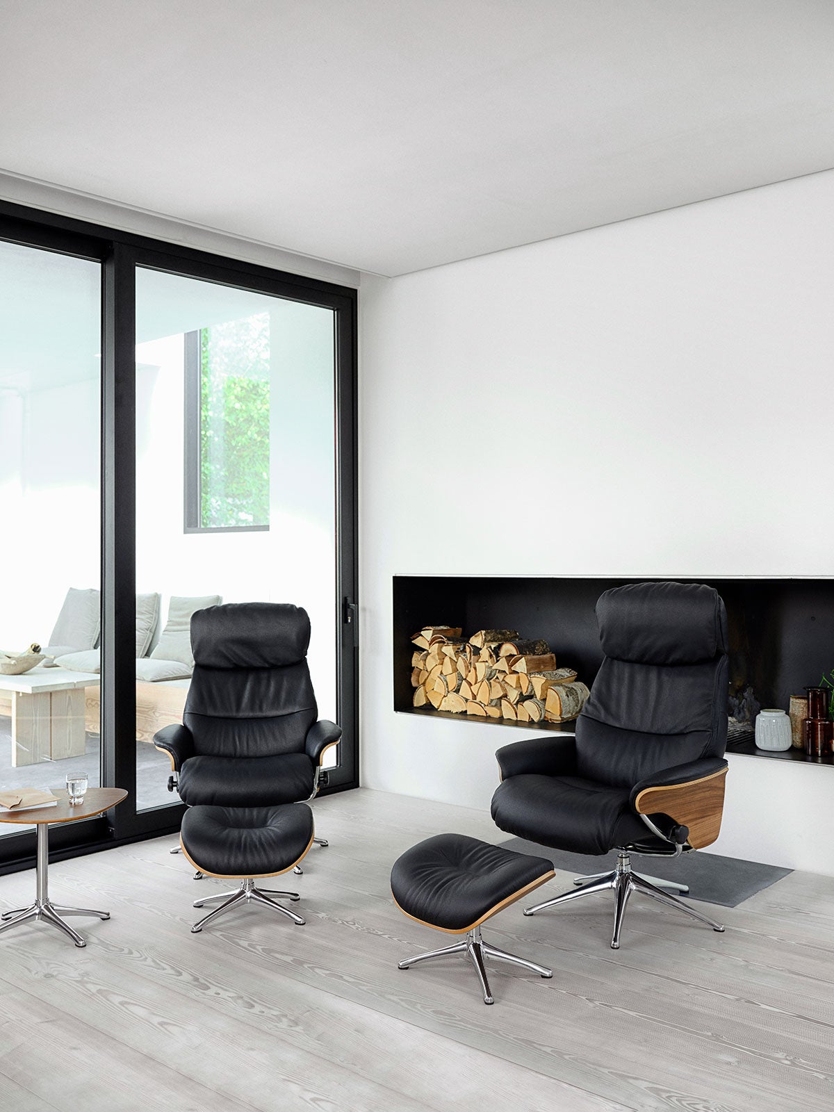 Aarhus Fåtölj och fotpall med fanérsidor i lädret Savoy i färgen Platin Black framför vedförvaring